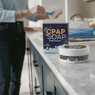 Person cleaning their CPAP in the sink with CPAP Soap in the foreground on the counter